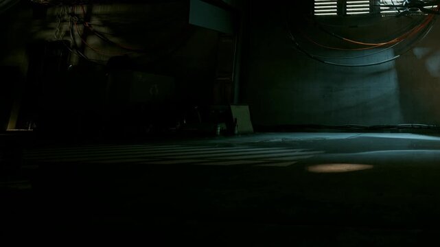A small patch of light shines on the ground in a dimly lit parking area. The walls are dark and show wires and pipes. The scene has an industrial feel and suggests nighttime.