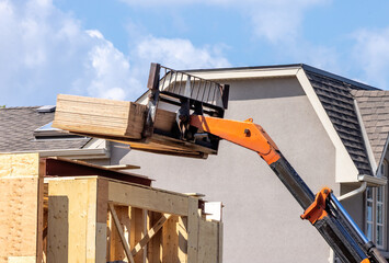 A boom forklift hoisting sheets of plywood to the roof of a construction site © SockaGPhoto