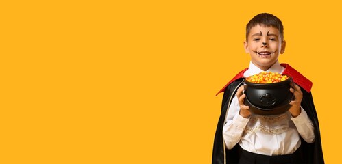 Naklejka premium Halloween celebration and trick or treat, happy boy in vampire costume holding candy corn in a black cauldron on a yellow background