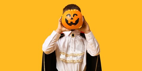 Naklejka premium Halloween celebration and childhood fun, child in vampire costume holding a jack-o'-lantern candy bucket on a bright yellow background