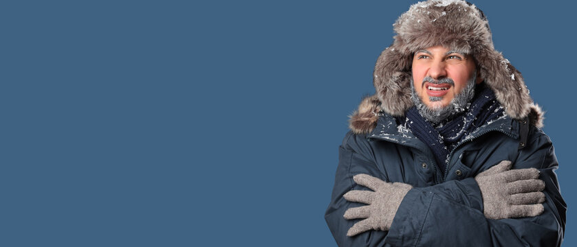 Extreme cold weather and energy crisis, man shivering in winter clothing with frost on beard and fur hat feeling freezing temperatures in blue background