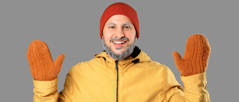 Winter fashion and seasonal joy, happy man wearing warm beanie and knitted mittens with frost on eyebrows in cold weather clothing on grey background