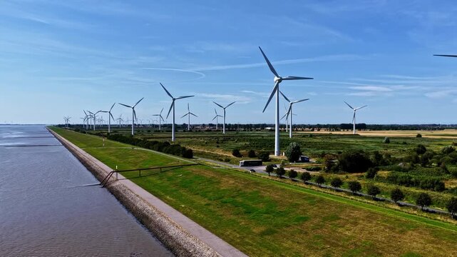 Aerial view of wind turbines along the coast with a green embankment and water in Emden, Niedersachsen, Germany.