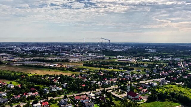 Aerial view of Orlen Plock Production Plant with industrial chimneys and smoking stacks rising above the surrounding residential area and green fields in Plock, Mazowieckie Voivodeship, Poland.