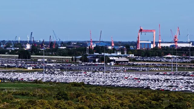 Aerial view of the Volkswagenwerk Emden automotive plant with rows of new cars parked in the lot and industrial cranes in the background in Emden, Niedersachsen, Germany.