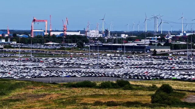 Aerial view of Volkswagenwerk Emden factory with vast rows of parked cars and wind turbines in the background in Emden, Niedersachsen, Germany.