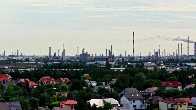 Aerial view of the Orlen Plock Production Plant with industrial chimneys and infrastructure rising above the surrounding residential neighborhood in Plock, Mazowieckie, Poland.