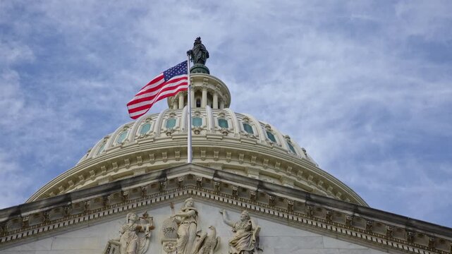 American flag waving on US Capitol. American flag in clouds over Capitol dome. American flag symbol of Amerika freedom. American flag on historic Capitol in Washington DC.