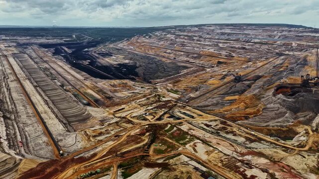 Aerial view of the massive Tagebau Hambach open-pit mine showing deep excavation terraces, heavy mining machinery, and vast industrial landscape in Elsdorf, Nordrhein-Westfalen, Germany.