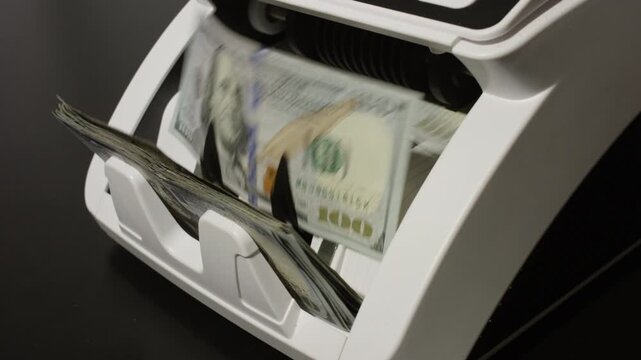 Money counting machine processing dollar bills in motion. Banking operation and finance concept with money movement. Counting money in motion. Counting dollar notes in a banking machine.