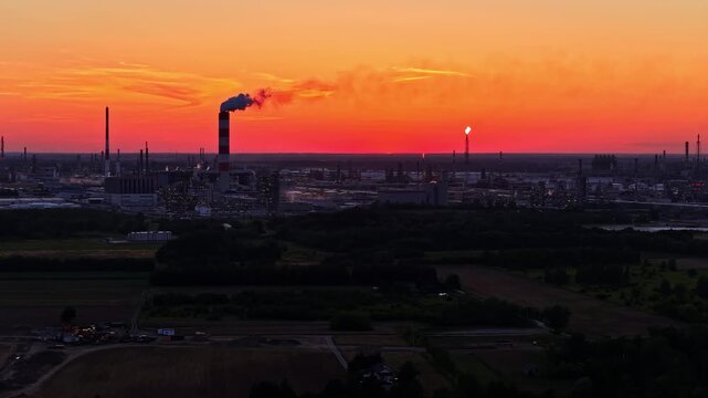 Aerial view of ORLEN Plock Production Plant with smoking chimney and flare stack under vibrant sunset sky in Plock, Mazowieckie, Poland.