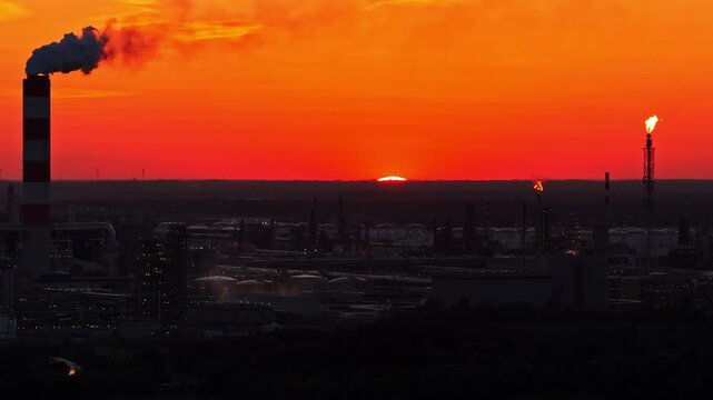 Aerial view of Orlen Plock Production Plant with industrial chimneys and flares glowing against a vibrant sunset sky in Plock, Mazowieckie, Poland.
