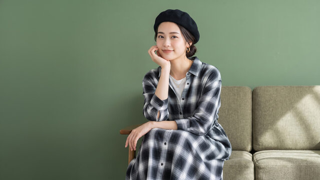 緑の壁の前にソファでくつろぎ微笑むチェック柄ワンピースを着た女性