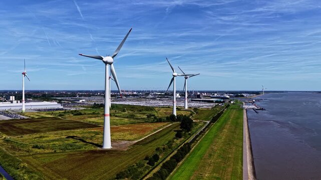 Aerial view of wind turbines at the Volkswagenwerk Emden factory grounds with industrial buildings and green fields near the river in Emden, Niedersachsen, Germany.
