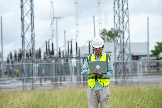 Engineer workout at electrical substation using laptop outdoors, wearing safety equipment and concentrating on field inspection work