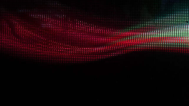 Extreme close-up macro shot of a digital display screen revealing a glowing RGB pixel grid in vibrant red and green colors fading into a dark black background.