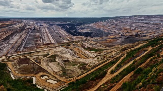 Aerial view of the massive Tagebau Hambach open-pit mine with industrial excavation machinery and terraced landscape under a cloudy sky in Elsdorf, Nordrhein-Westfalen, Germany.