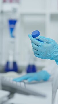 Close-up of a laboratory professional holding a sample vial while typing on a computer during data review and laboratory analysis.
