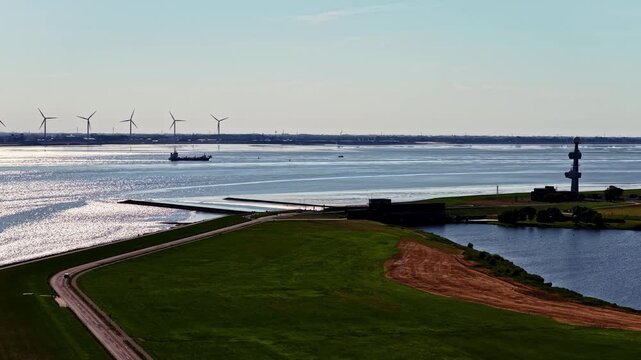Aerial view of the Ems estuary with wind turbines, a cargo ship, and coastal dikes in Emden, Niedersachsen, Germany.