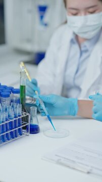 Laboratory technician using a pipette to drop liquid sample into a petri dish during microbiology testing in a clean research laboratory.