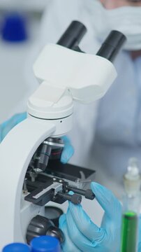 Laboratory technician adjusting a microscope for sample examination in a clean medical laboratory environment with precision equipment and protective gloves.