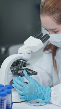 Medical laboratory professional observing a sample through a microscope during routine analysis in a clean research setting with clinical equipment.