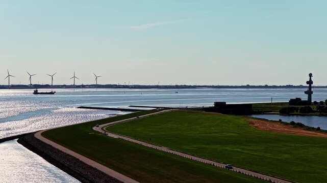 Aerial view of the Ems estuary with wind turbines, a cargo ship, and coastal landscape near Emden, Niedersachsen, Germany.
