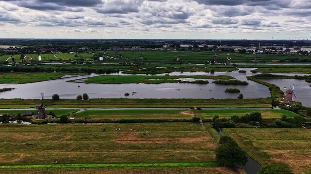 Aerial view of the historic Kinderdijk windmills set amidst lush green polders, winding canals, and dramatic cloudy skies in Kinderdijk, Zuid-Holland, Netherlands.