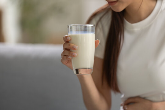 Lactose intolerance concept. woman holding glass of milk while touching her stomach at home, suggesting dairy sensitivity and digestive discomfort. lactose, milk, woman, dairy, health.