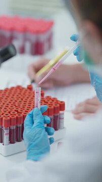 Laboratory professional transferring blood sample into a test tube with a pipette in a bright clinical laboratory setting.
