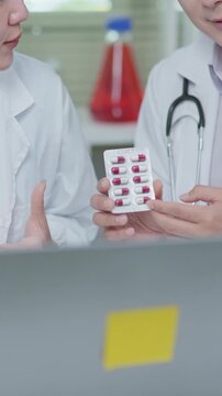 Doctor showing blister pack and explaining medication during an online medical consultation with laptop in clinic setting.