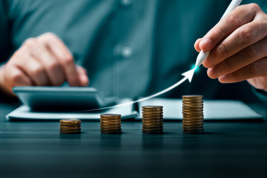 Financial growth concept with hand using stylus on rising arrow over stacked coins showing investment revenue increase profit planning and business success strategy