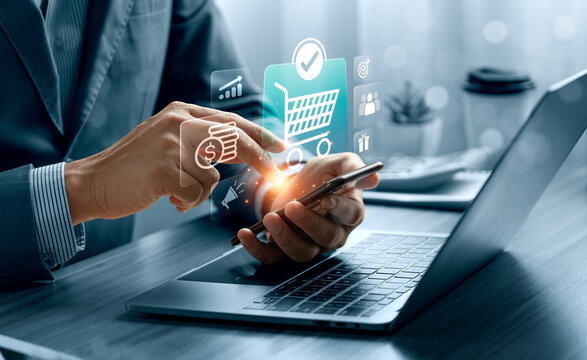 Mobile shopping concept with business professional using smartphone beside laptop showing virtual shopping cart interface, online payment, purchase approval and ecommerce service