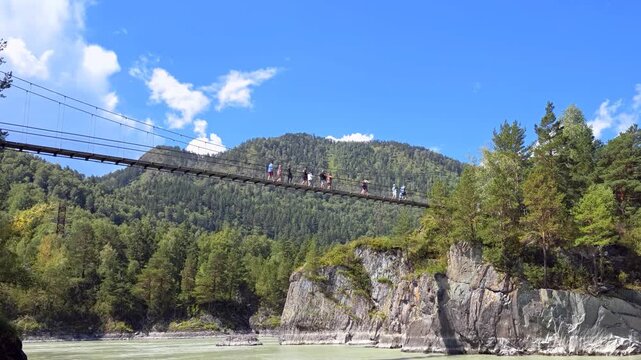 Slow motion video of people are walking along hinged bridge to the island of Patmos over river Katun in Altai.