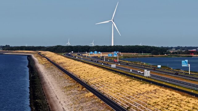 Aerial view of the Windpark Fryslan wind turbine towering over the Afsluitdijk highway and surrounding water in Breezanddijk, Friesland, Netherlands.