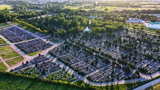 Aerial view of a large cemetery with rows of graves and trees surrounded by green fields in Plock, Mazowieckie, Poland.