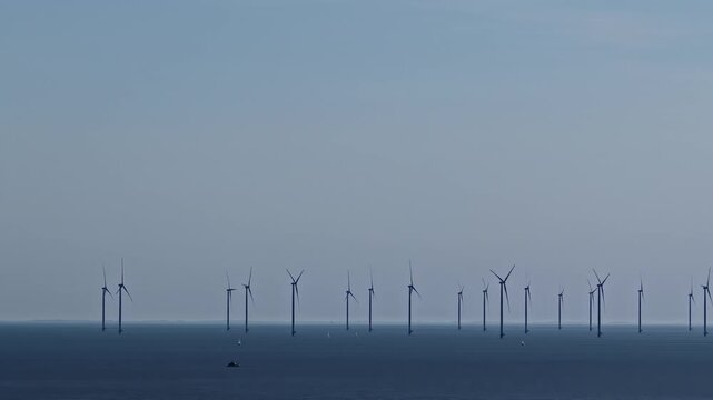 Aerial view of Windpark Fryslan offshore wind turbines standing in the sea under a clear blue sky near Breezanddijk, Friesland, Netherlands.