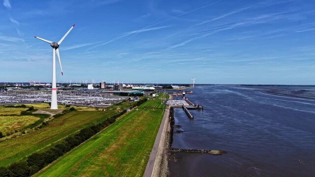 Aerial view of the Volkswagenwerk Emden factory with wind turbines, rows of parked cars, and the Ems river in Emden, Niedersachsen, Germany.