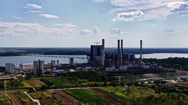Aerial view of the ZE PAK SA Patnow Power Plant with its tall chimneys and industrial structures situated near a large lake and surrounded by green fields in Konin, Wielkopolskie, Poland.