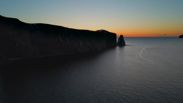 Dramatic cliff face and sea stack bathed in twilight glow aerial drone footage.