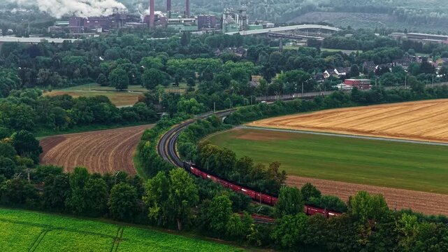 Aerial view of a train traveling through green fields and lush trees near the RWE Power AG power plant Niederaussem in Bergheim, Nordrhein-Westfalen, Germany.