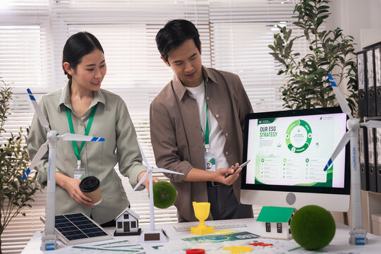 esg concept, Asian business partners reviewing sustainable energy strategy with wind turbine model and environmental report modern office, expressing focused collaboration and optimism about renewable