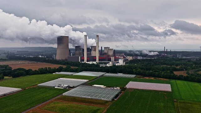 Aerial view of RWE Power AG power plant Niederaussem with cooling towers emitting steam over surrounding agricultural fields and greenhouses in Bergheim, Nordrhein-Westfalen, Germany.