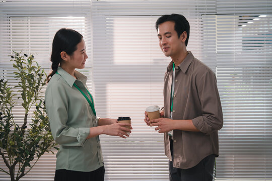 esg concept, Office colleagues discussing work while holding takeaway coffee near window blinds, creating relaxed professional workplace conversation during short break