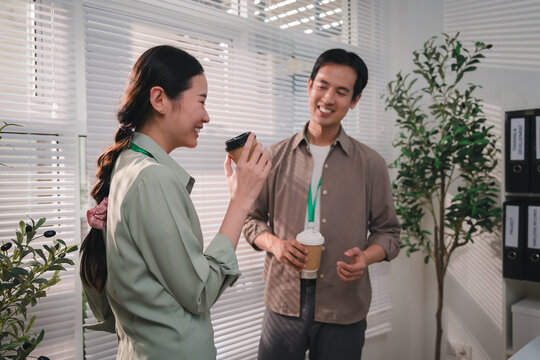 esg concept, Asian business colleagues discussing mobile phone in modern office with warm smiles and natural workplace interaction