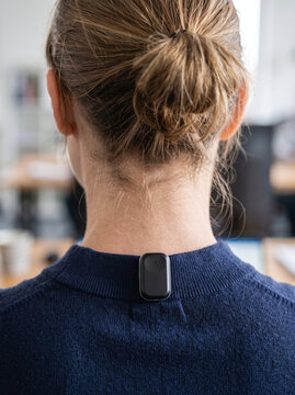 Woman wearing smart posture tracking sensor clipped on shirt collar in office