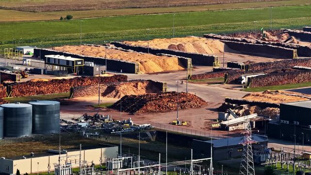 Aerial view of industrial wood processing facility with large piles of wood chips and storage tanks in Suwalki, Podlaskie Voivodeship, Poland.