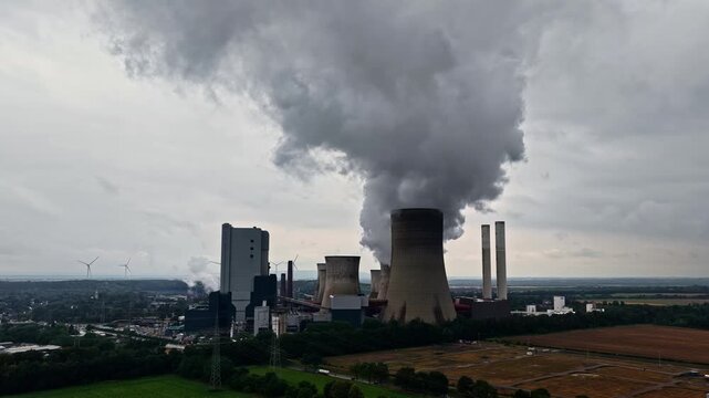 Aerial view of RWE Power AG power plant Niederaussem with cooling towers emitting steam under a cloudy sky in Bergheim, Nordrhein-Westfalen, Germany.