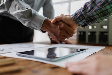 Business partners shaking hands over architectural blueprints and digital tablet, confirming agreement and cooperation for construction project development © groviapoto