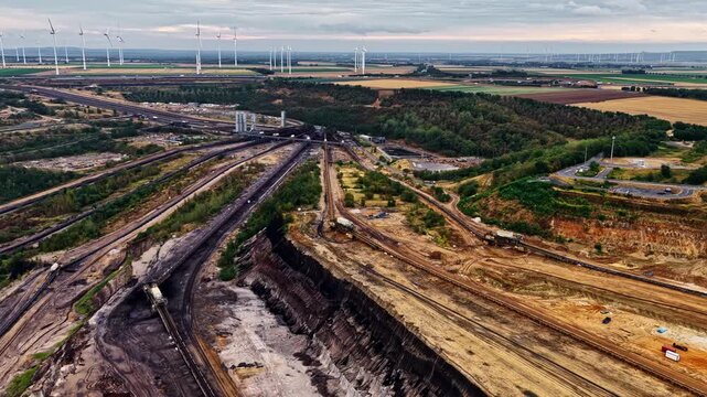 Aerial view of Garzweiler surface mine showing extensive open-pit mining operations with industrial tracks and wind turbines in the background in Juchen, North Rhine-Westphalia, Germany.